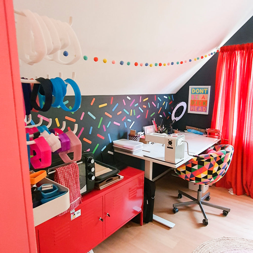 Creative home studio space of polymerclay and resin earring artist. Bright colours, sprinkles decals on a navy wall, colourful geometric patterned chair.